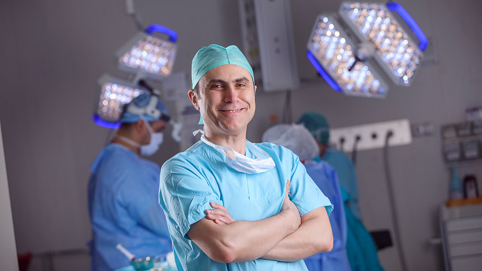 Experienced surgeon portrait in operating room with medical team and surgical lights in the background