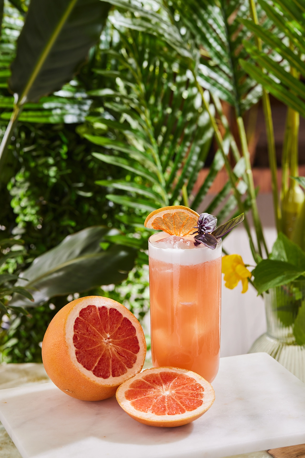 Fresh grapefruit beverage served with citrus slices in a tropical outdoor setting surrounded by lush greenery.