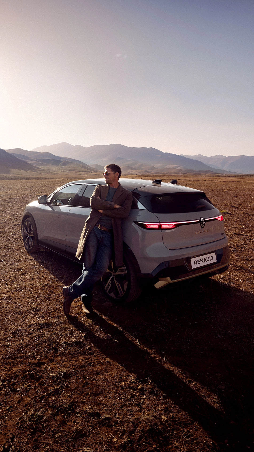 Renault Megane E-Tech electric vehicle and driver overlooking mountain landscape at sunset