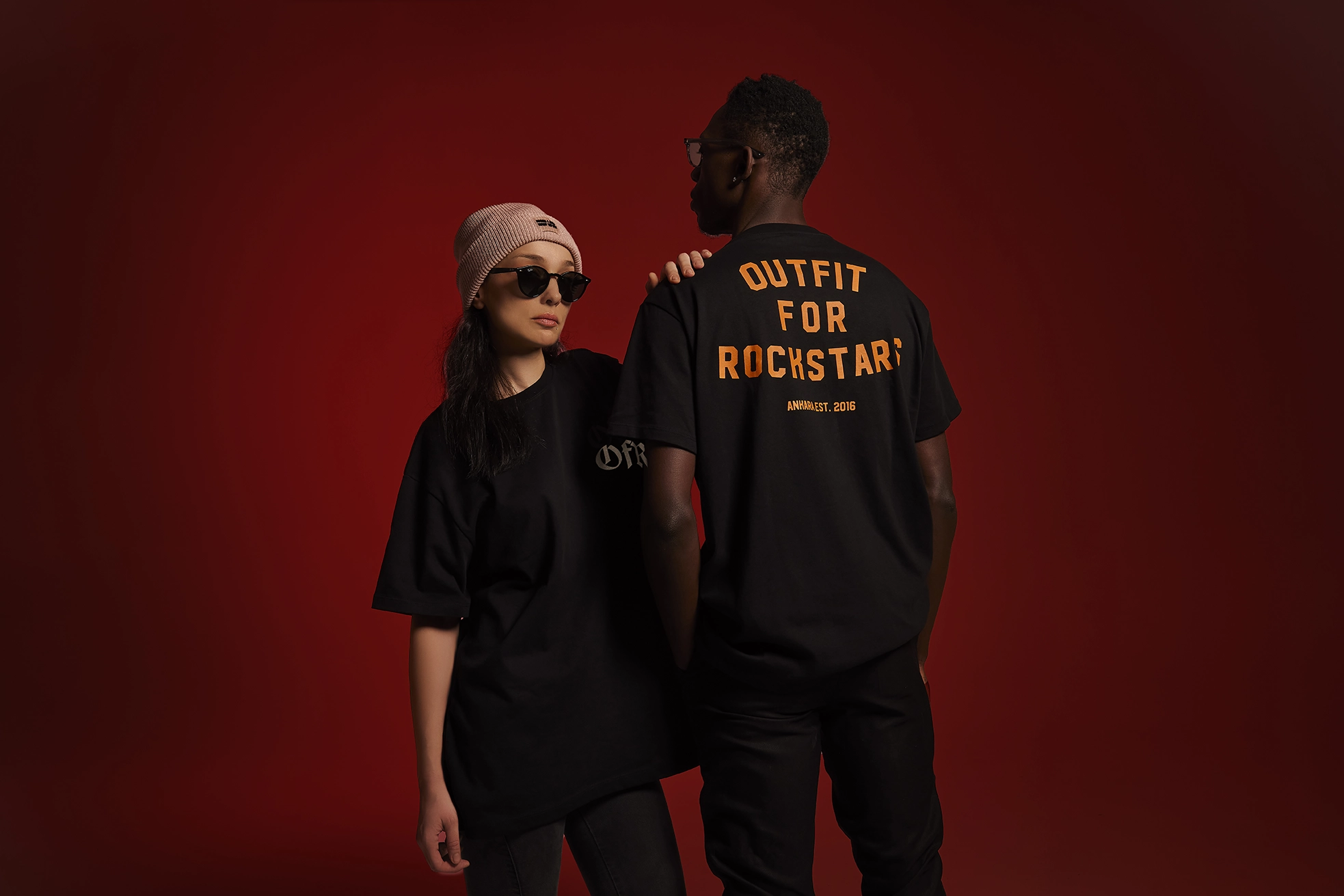 Two models wearing black streetwear t-shirts against a red studio background featuring a bold Power to the People design.