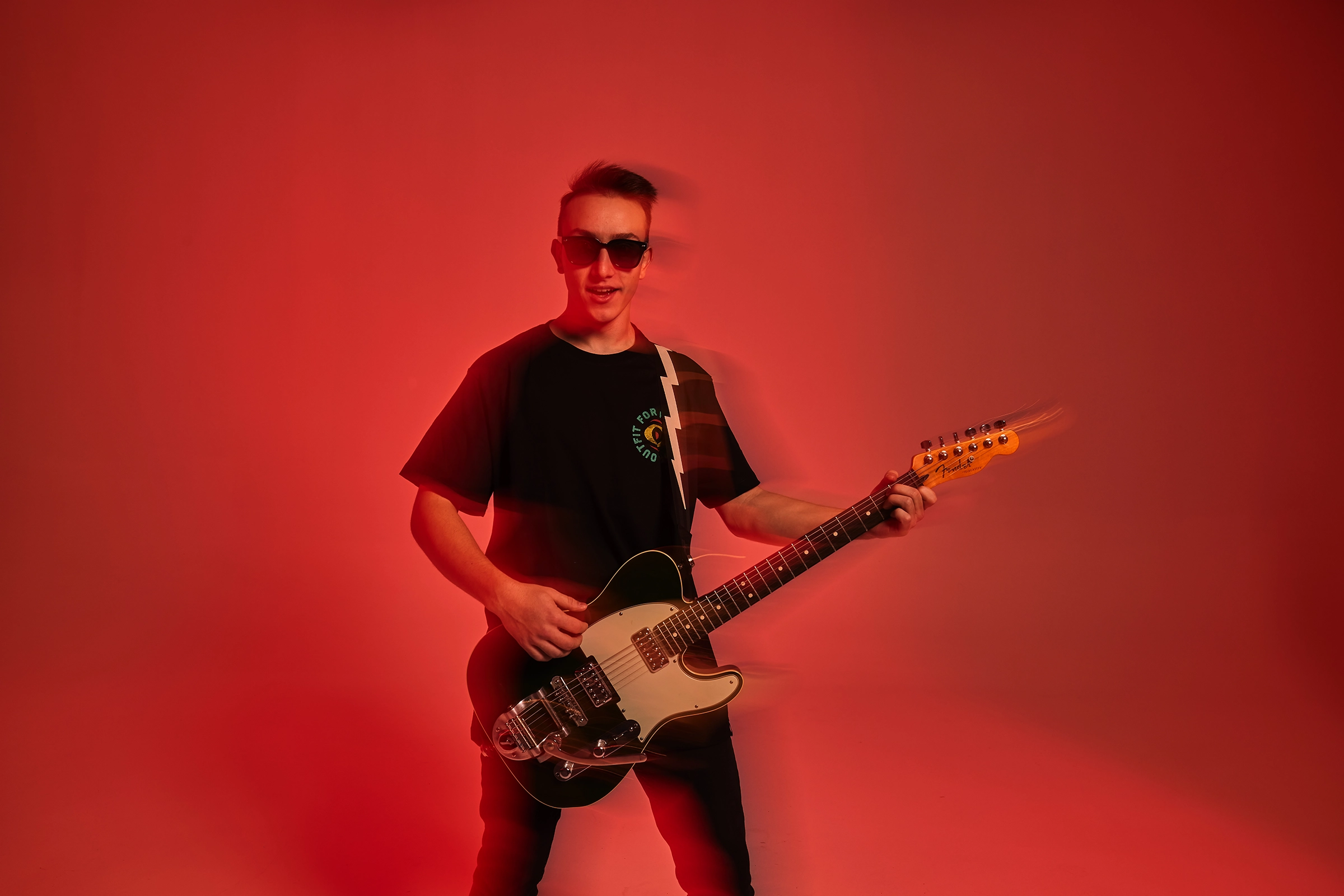 Male guitarist performing with an electric guitar against a dramatic red studio background.