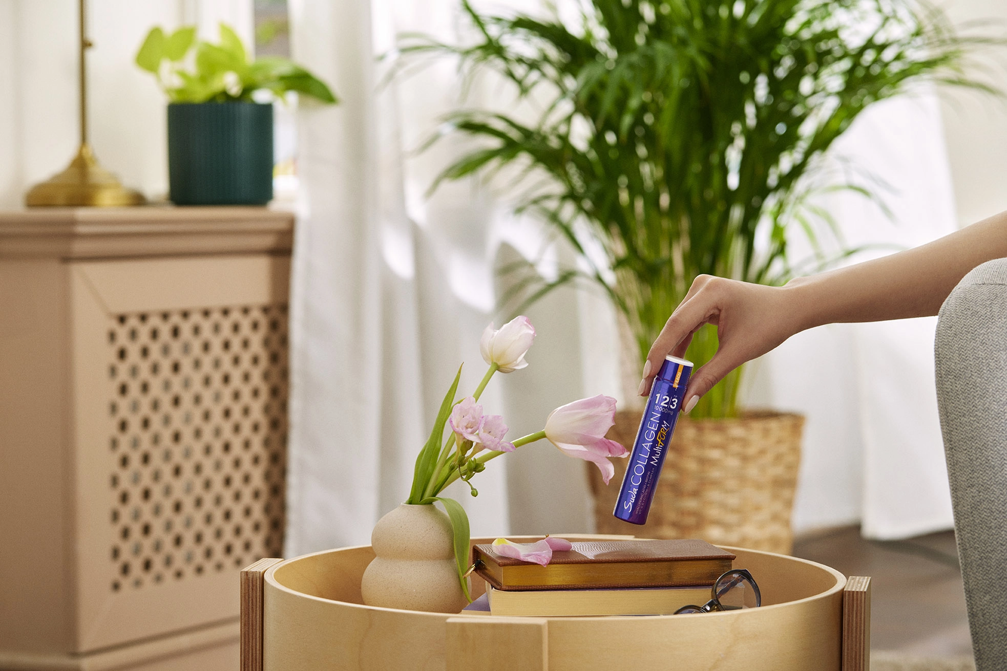 Hand placing a collagen supplement shot on a table in a bright home environment, wellness lifestyle concept.