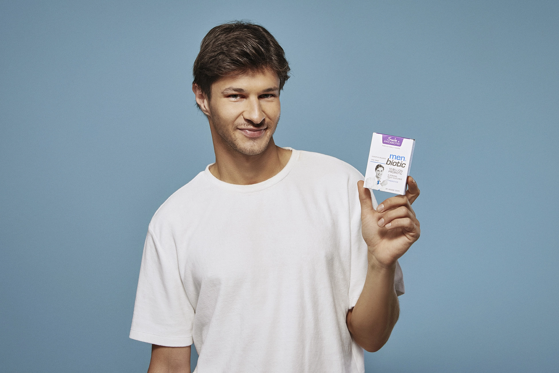 Male model holding a probiotic supplement product against a clean blue background in a healthcare advertising campaign.