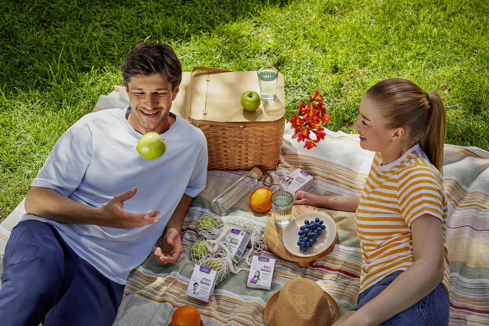 Couple enjoying a healthy picnic outdoors with probiotic supplements and fresh fruits in a lifestyle advertising campaign.