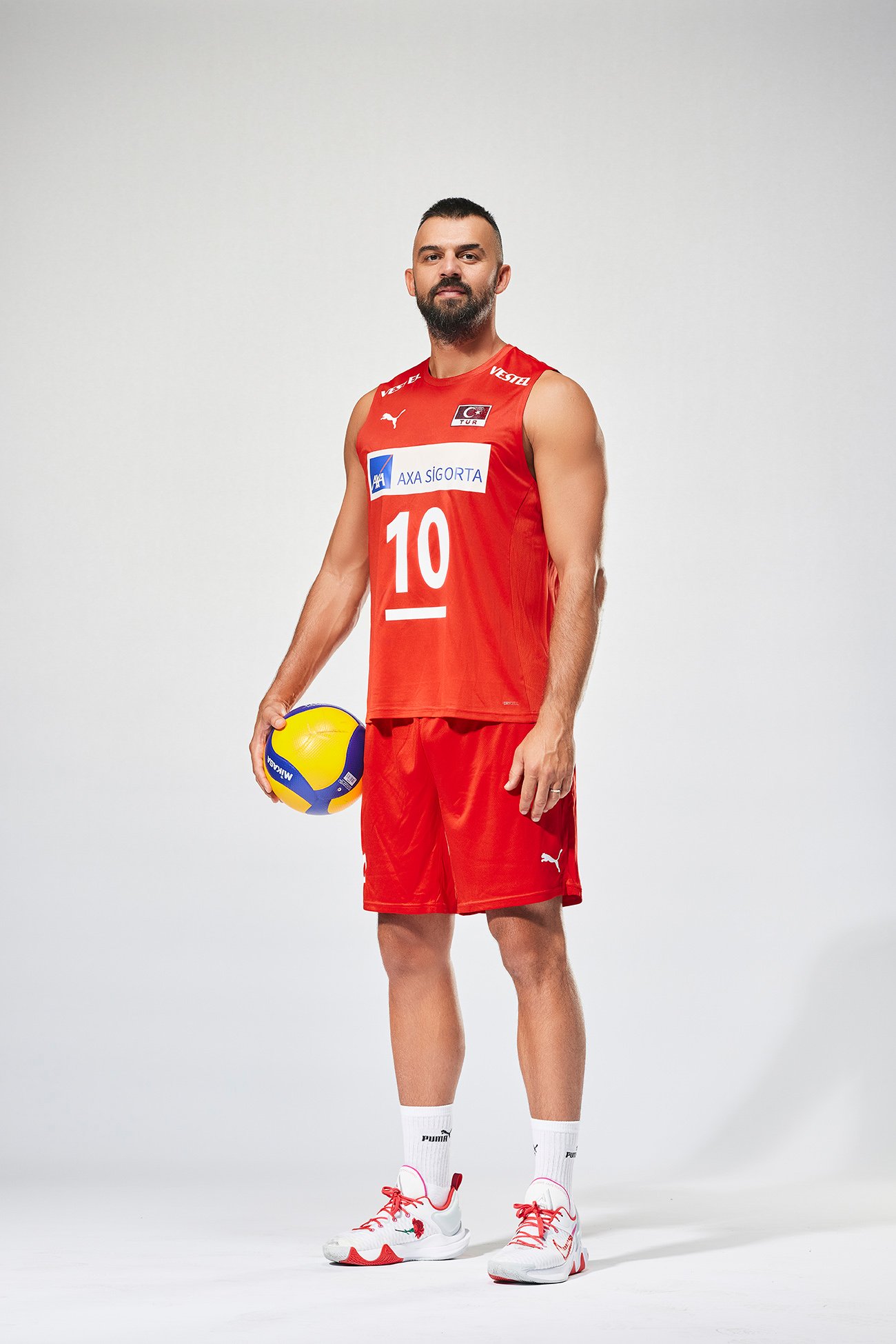 Studio portrait of Arslan Ekşi wearing the Türkiye Men’s National Volleyball Team uniform and holding a volleyball.