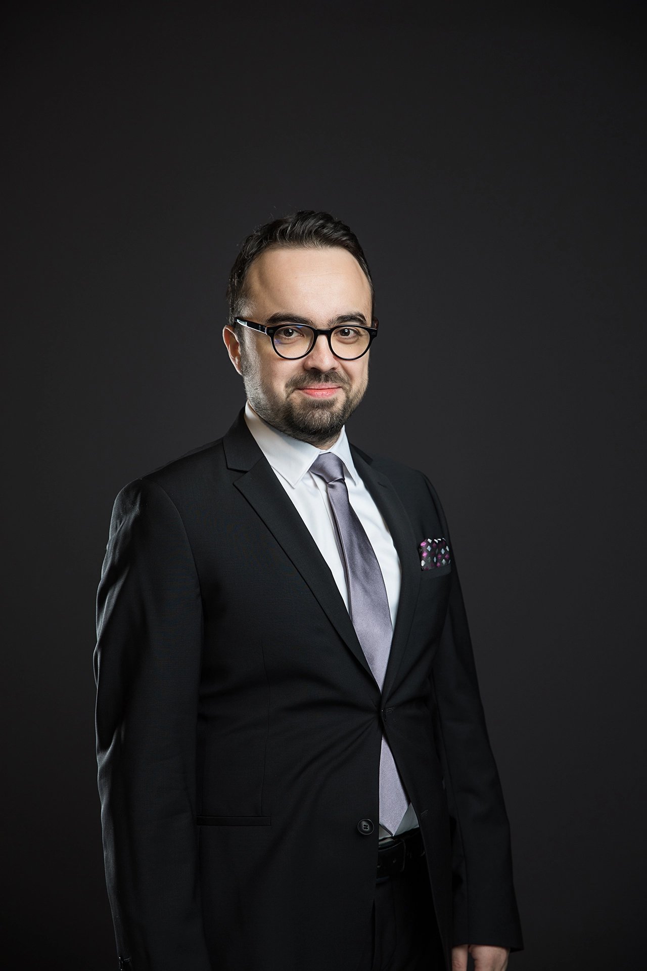 Professional studio portrait of a company team member photographed against a dark background with controlled lighting.