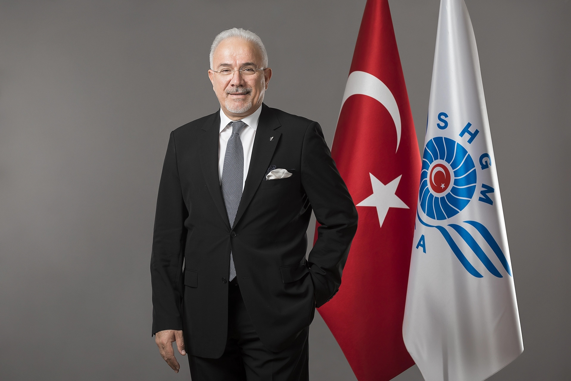 Executive portrait of a senior corporate leader standing beside institutional flags, photographed for corporate communications and leadership branding.