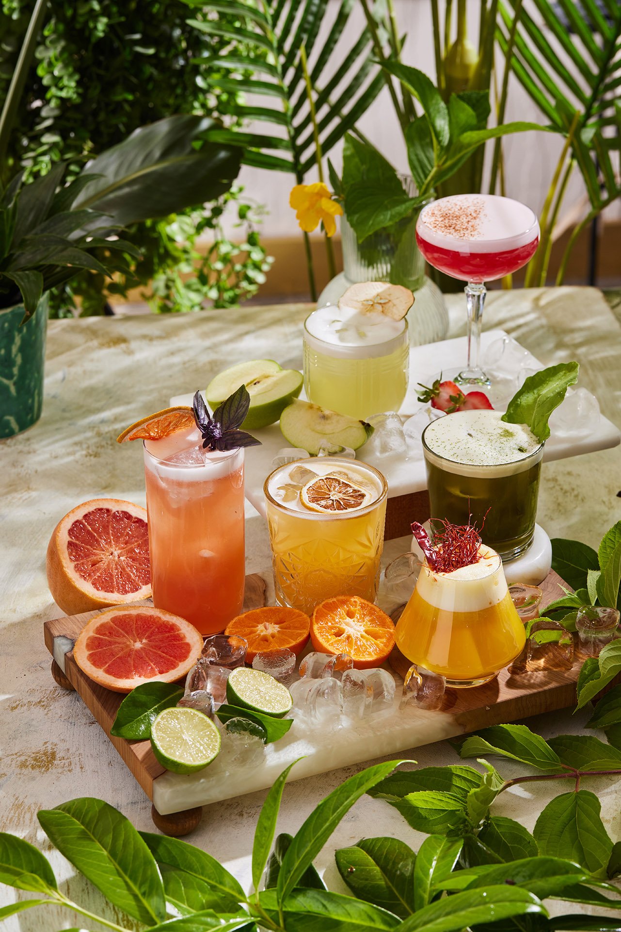 A stunning and rich commercial beverage photograph by Sinan Niyazi Kutsal for Barley Brasserie, displaying six different colorful artisan cocktails arranged on elegant serving boards with loose ice and fresh fruits.