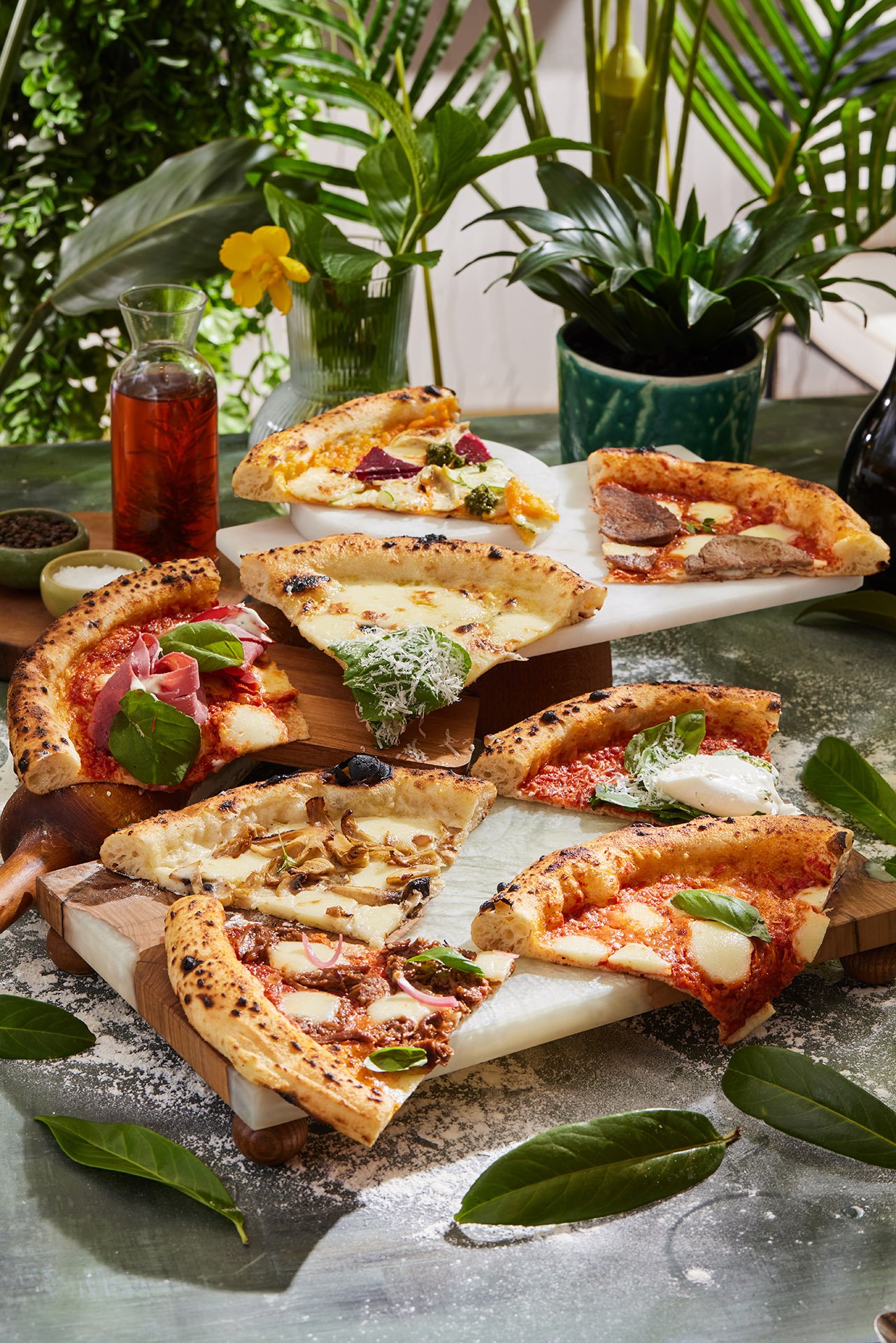 An incredible commercial food photograph by Sinan Niyazi Kutsal for Barley Brasserie, displaying an assortment of multiple different gourmet Neapolitan pizza slices on elevated marble and wood serving stands.