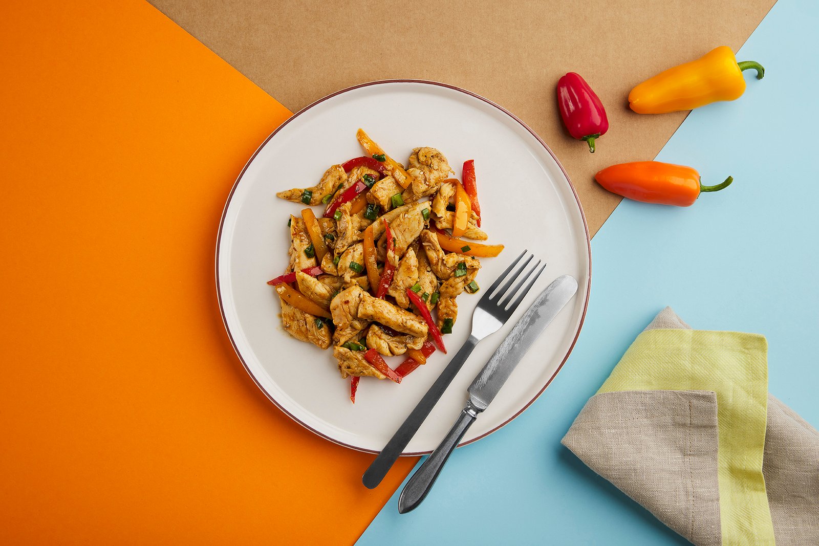 Professional commercial food advertising photograph by Sinan Niyazi Kutsal for Tarifte, featuring a wide top-down view of multiple plates of chicken, steak, and vegetables arranged around a large orange circular brand logo on white wood boards.