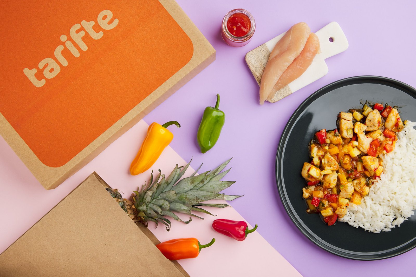 Professional commercial food advertising photograph by Sinan Niyazi Kutsal for Tarifte, featuring a wide top-down view of multiple plates of chicken, steak, and vegetables arranged around a large orange circular brand logo on white wood boards.