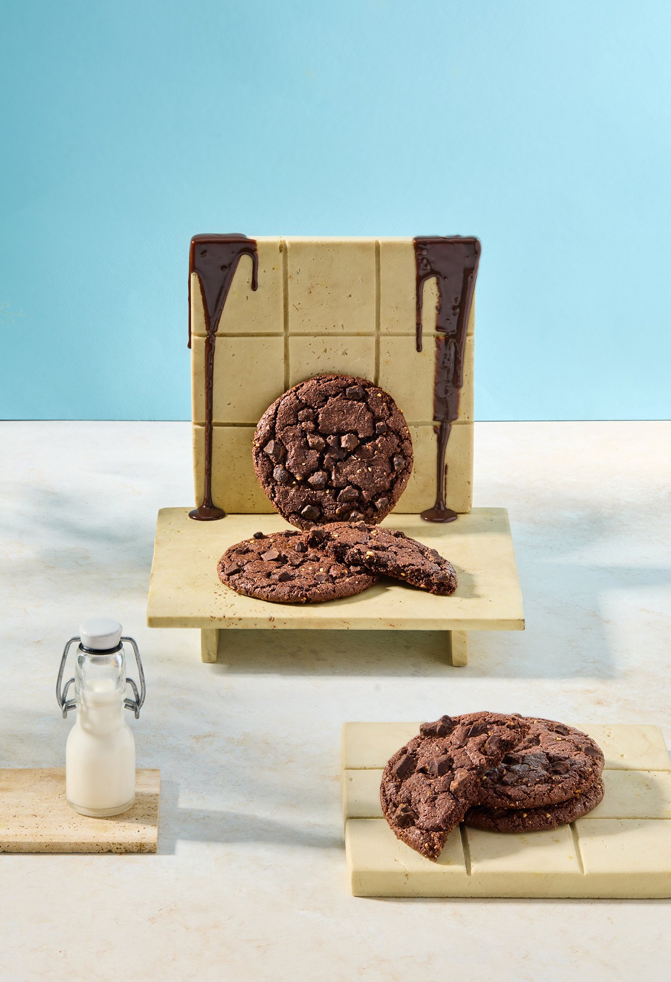 Studio photograph of Simit Sarayı chocolate cookies displayed with white chocolate, milk bottle and chocolate drizzle under hard daylight-style flash lighting.
