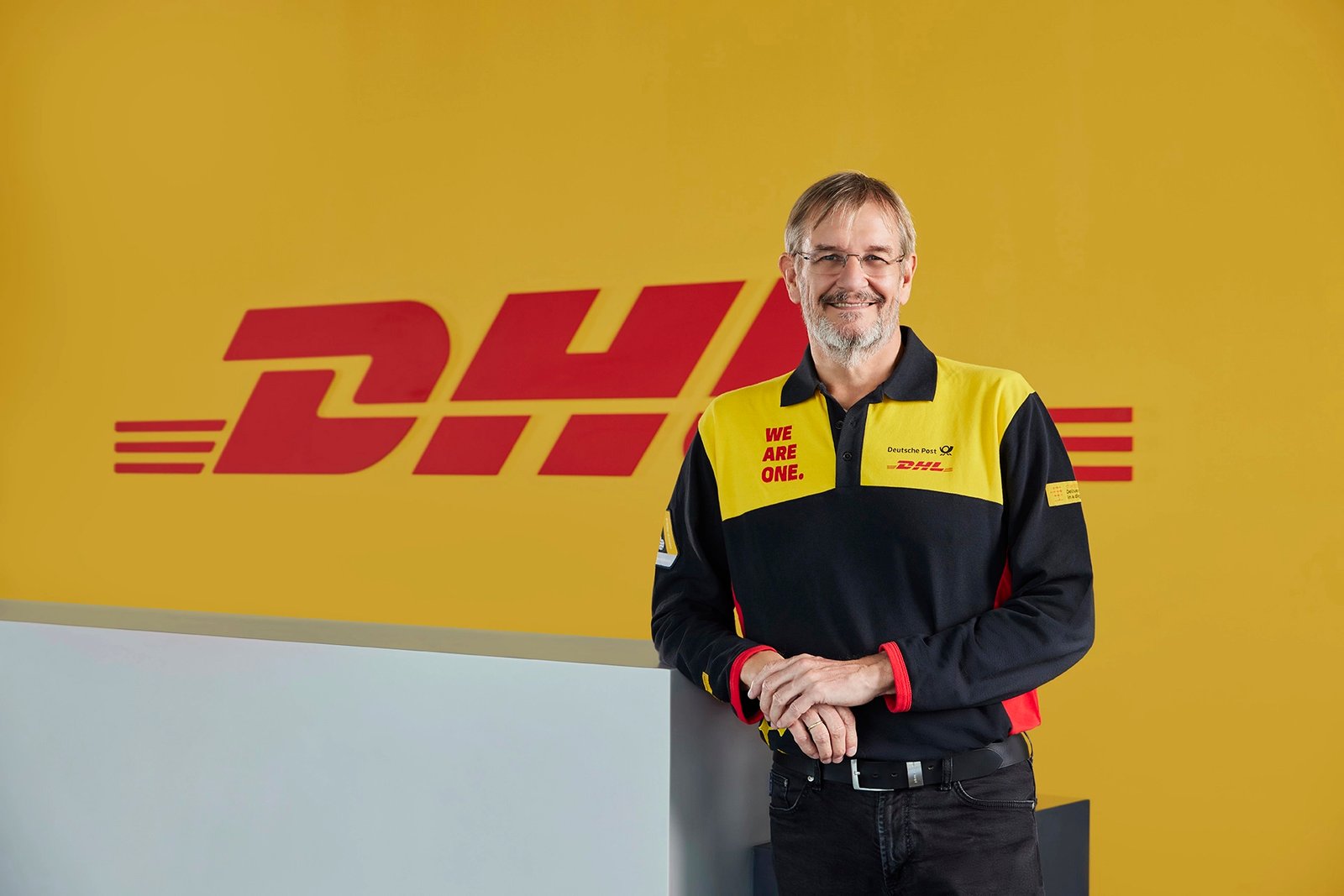 DHL Türkiye General Manager posing for a corporate portrait in front of a yellow DHL branded wall.