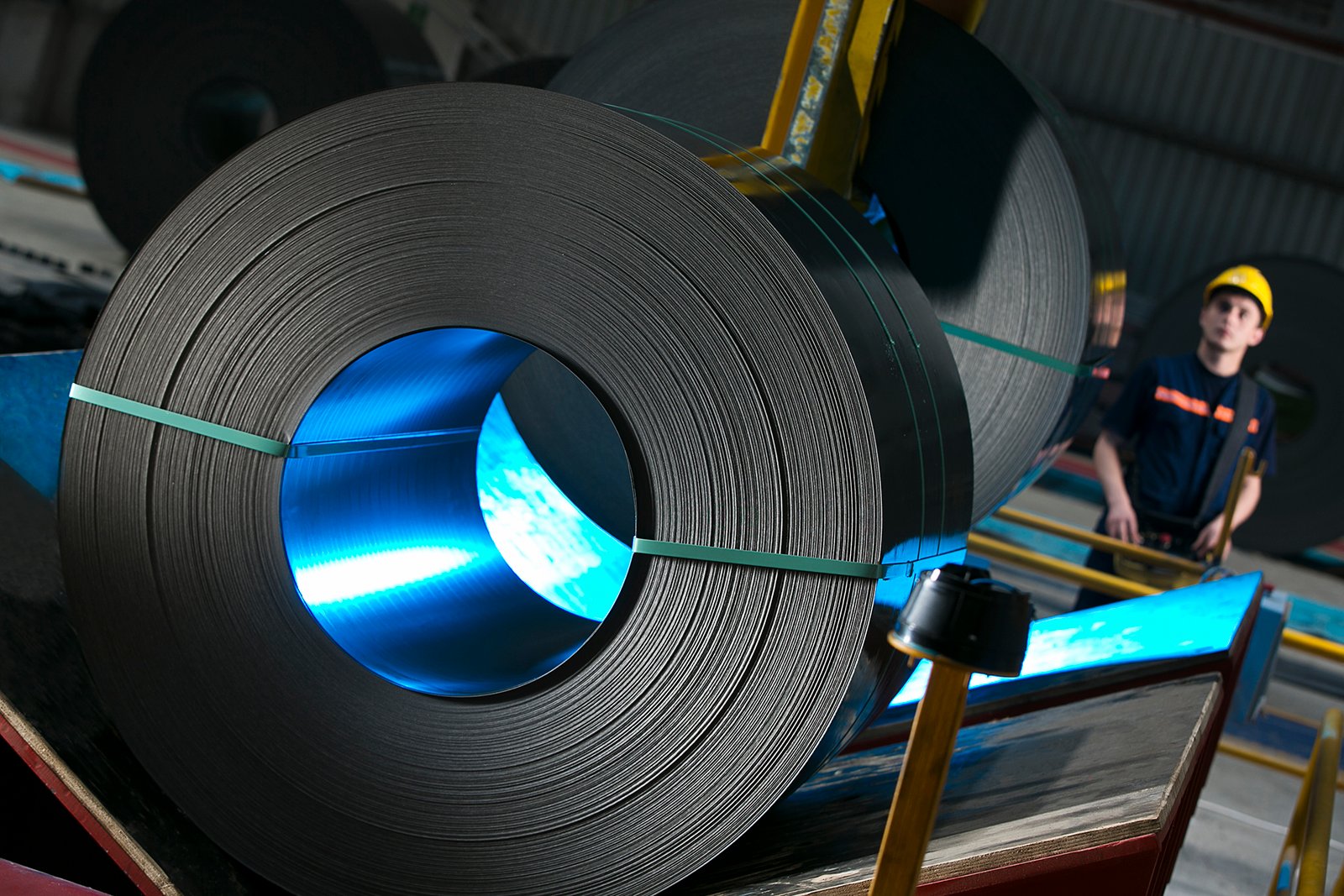 Professional commercial industrial photographs by Sinan Niyazi Kutsal for Gazi Metal capturing plant engineers operating automated console panels, a large overhead crane hoist picking up a steel coil, and rows of metal sheets in a warehouse.