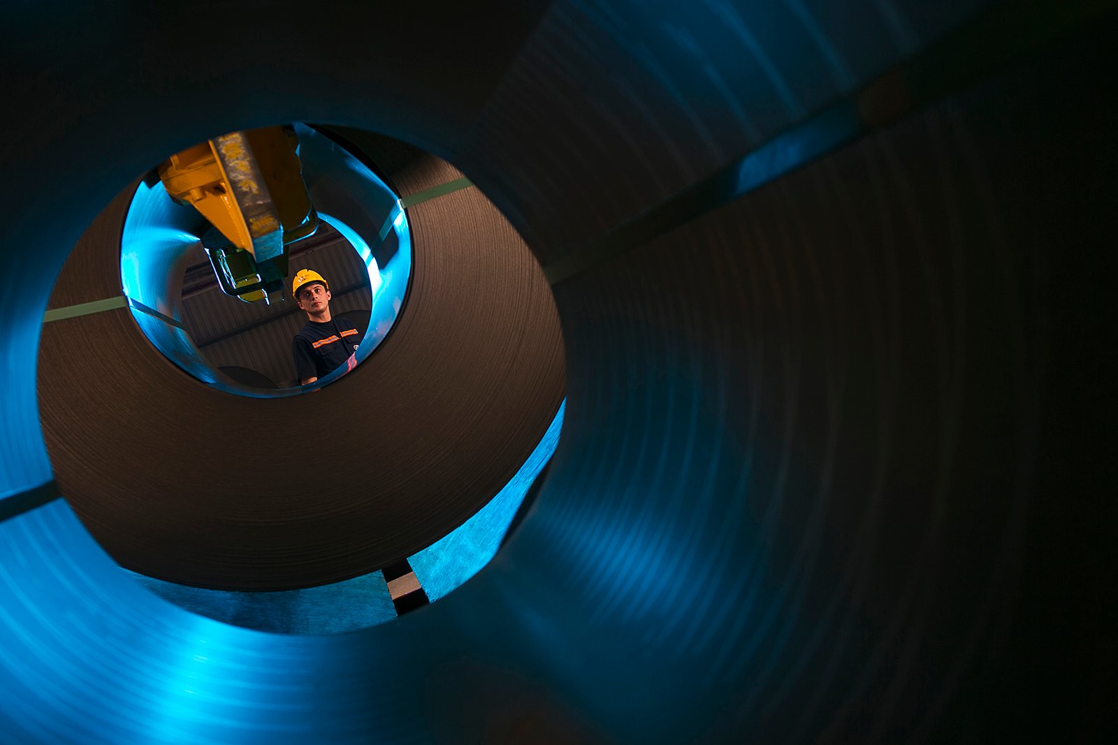 Professional commercial industrial photographs by Sinan Niyazi Kutsal for Gazi Metal, capturing manufacturing plant operators inspecting immense rolls of steel sheeting using radio communication inside a Sakarya warehouse.