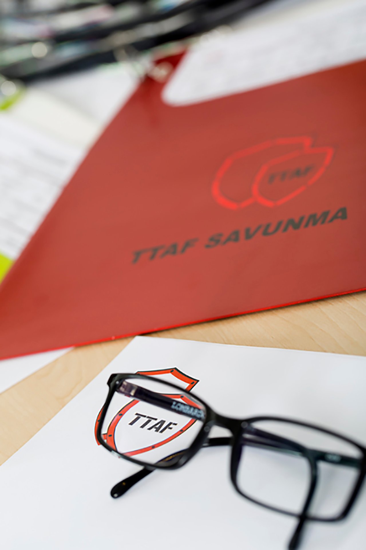 Professional commercial corporate photographs by Sinan Niyazi Kutsal for TTAF Savunma, capturing a soldier with a rifle and tech helmet next to laboratory engineers, and a tabletop setup of corporate folders, cable harnesses, and Turkish desk flags.