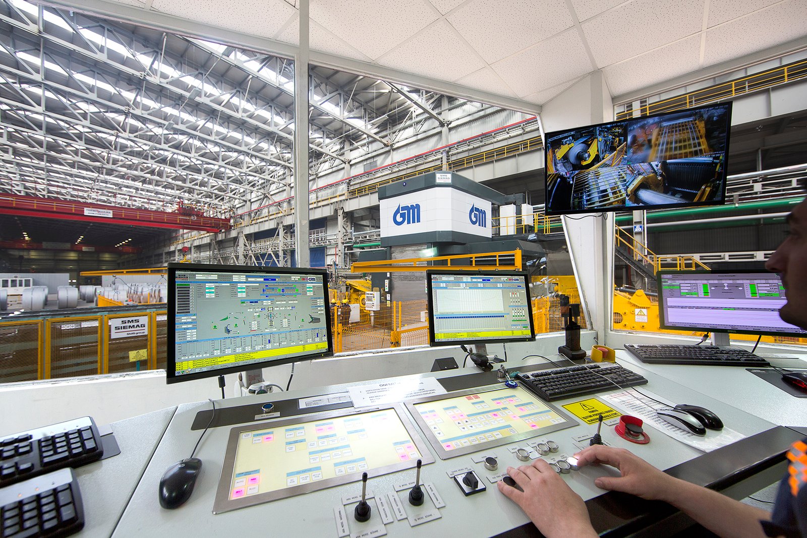 Professional commercial industrial photographs by Sinan Niyazi Kutsal for Gazi Metal capturing plant engineers operating automated console panels, a large overhead crane hoist picking up a steel coil, and rows of metal sheets in a warehouse.