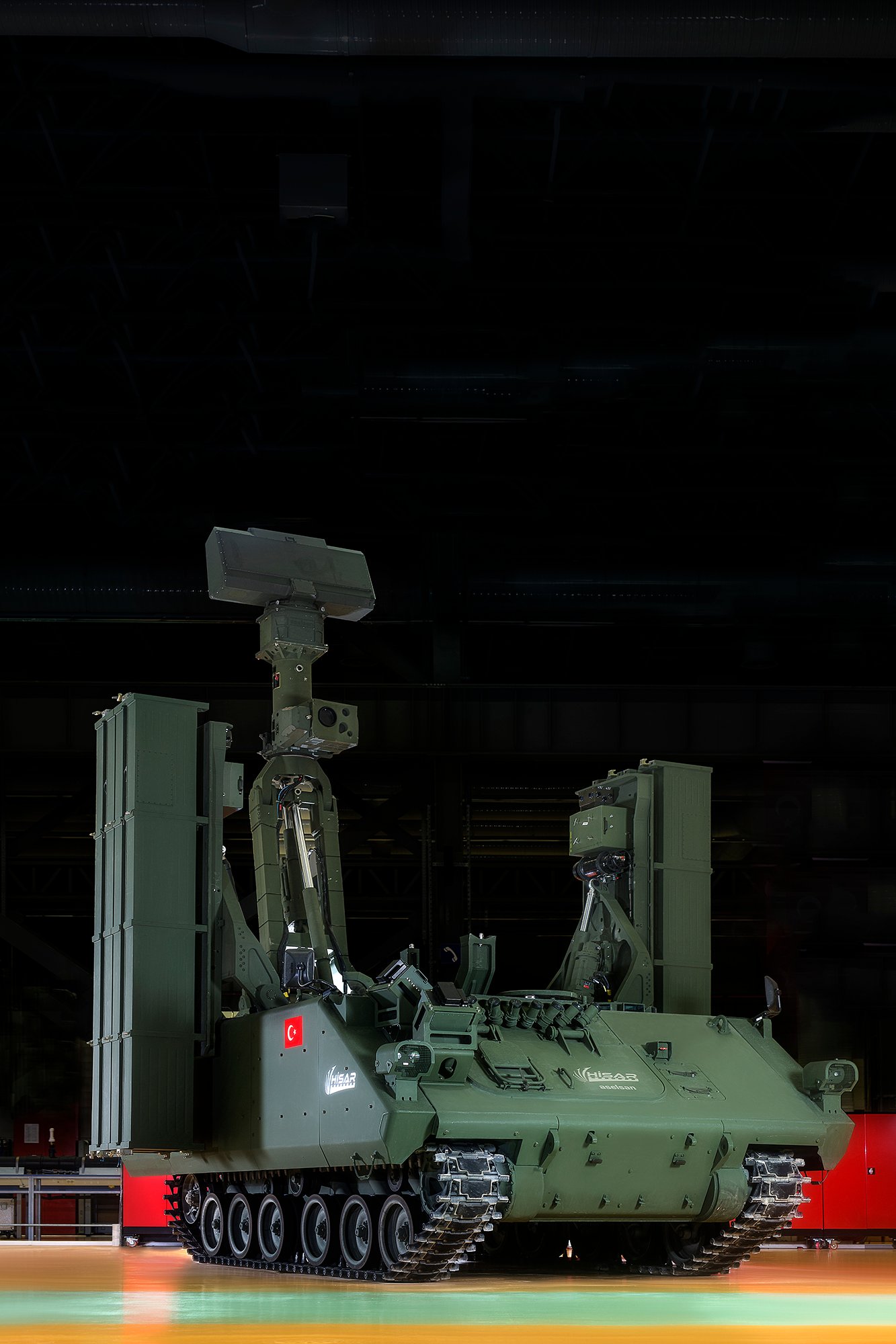 Professional commercial defense industry photograph by Sinan Niyazi Kutsal capturing the military green ASELSAN HISAR air defense missile vehicle equipped with radar and launchers inside a high-tech facility hangar.