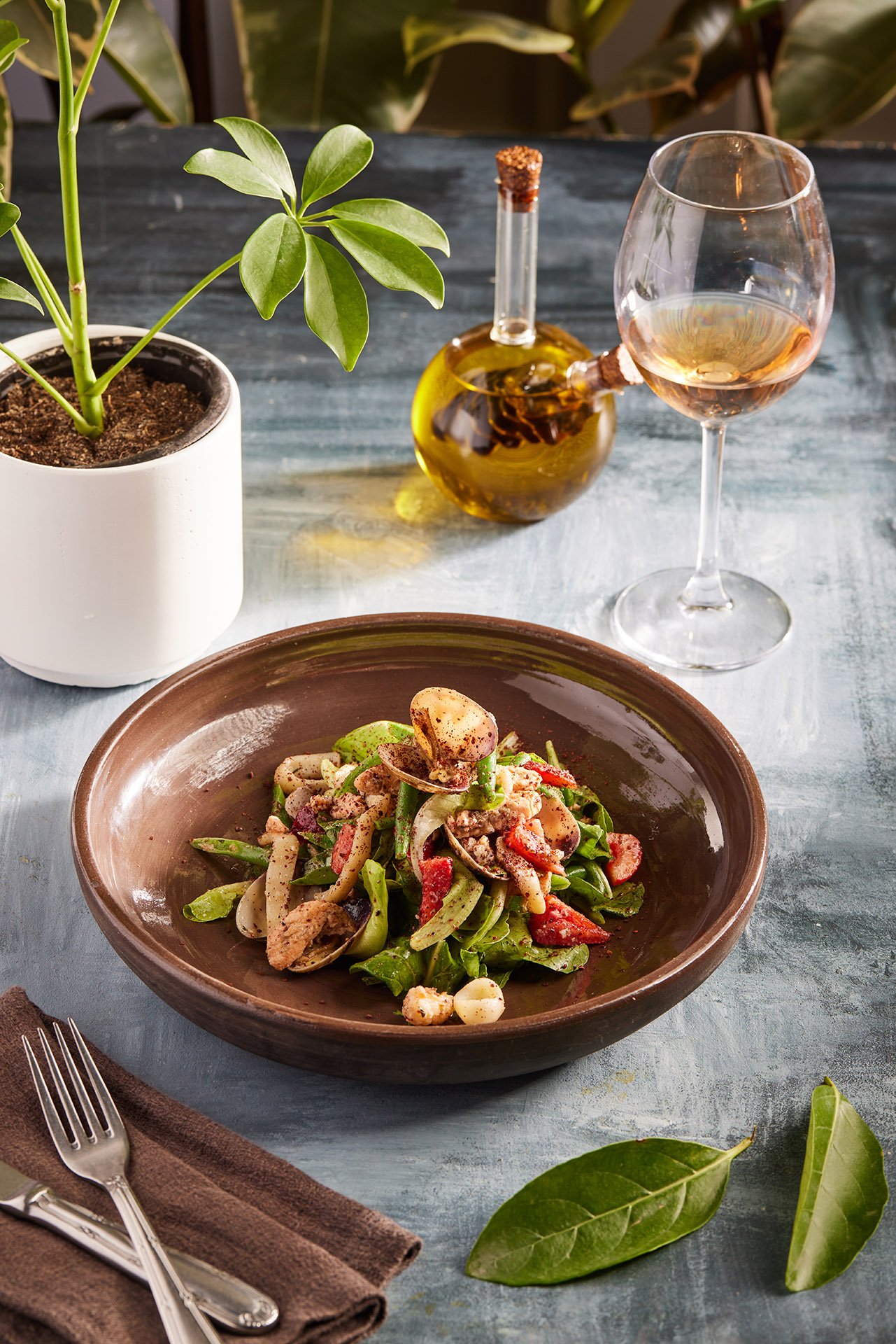 A beautiful commercial food photograph by Sinan Niyazi Kutsal for Barley Brasserie, showcasing an upscale seafood salad with clams and squid in a large brown ceramic bowl alongside a glass of white wine.