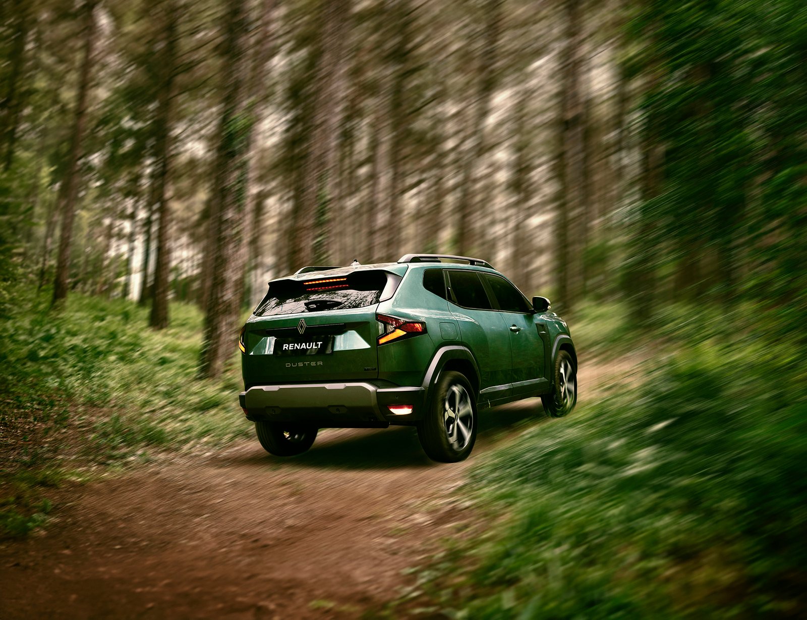 A professional commercial automotive photograph by Sinan Niyazi Kutsal featuring a grey Dacia Duster compact SUV parked on a rustic dirt road surrounded by green trees in Belgrad Forest.