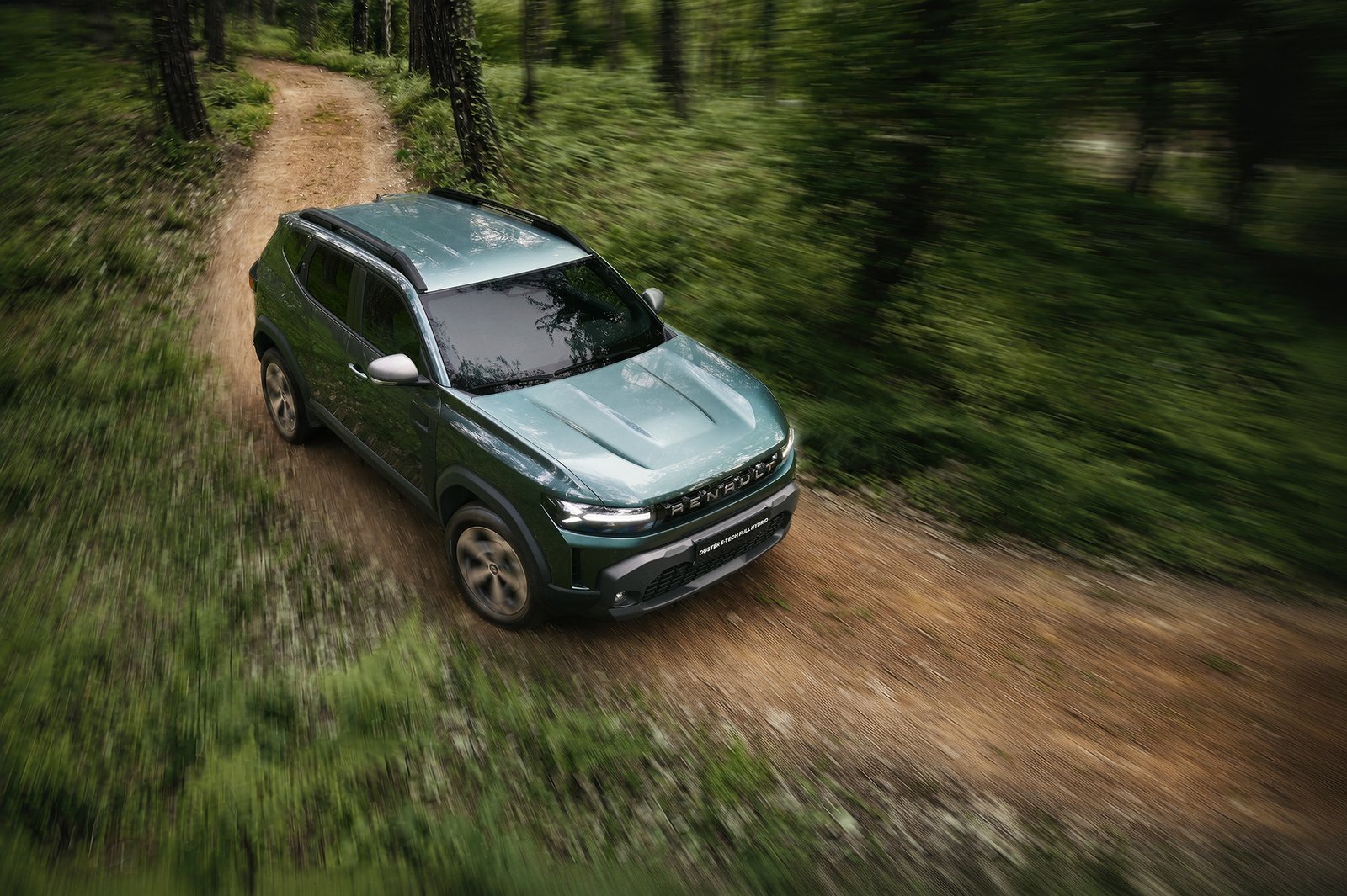 A professional commercial automotive photograph by Sinan Niyazi Kutsal featuring a grey Dacia Duster compact SUV parked on a rustic dirt road surrounded by green trees in Belgrad Forest.