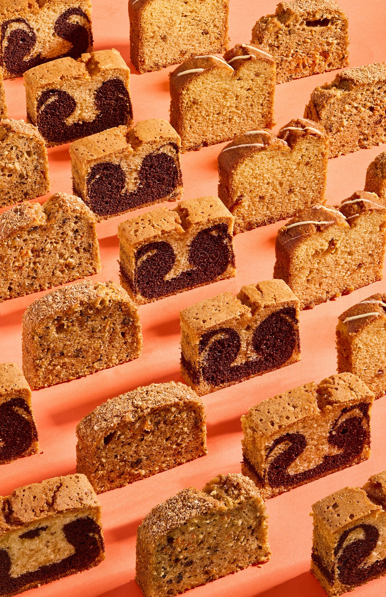 Studio photograph featuring a selection of Simit Sarayı loaf cakes and marble cakes arranged in a geometric pattern under hard daylight-style flash lighting.