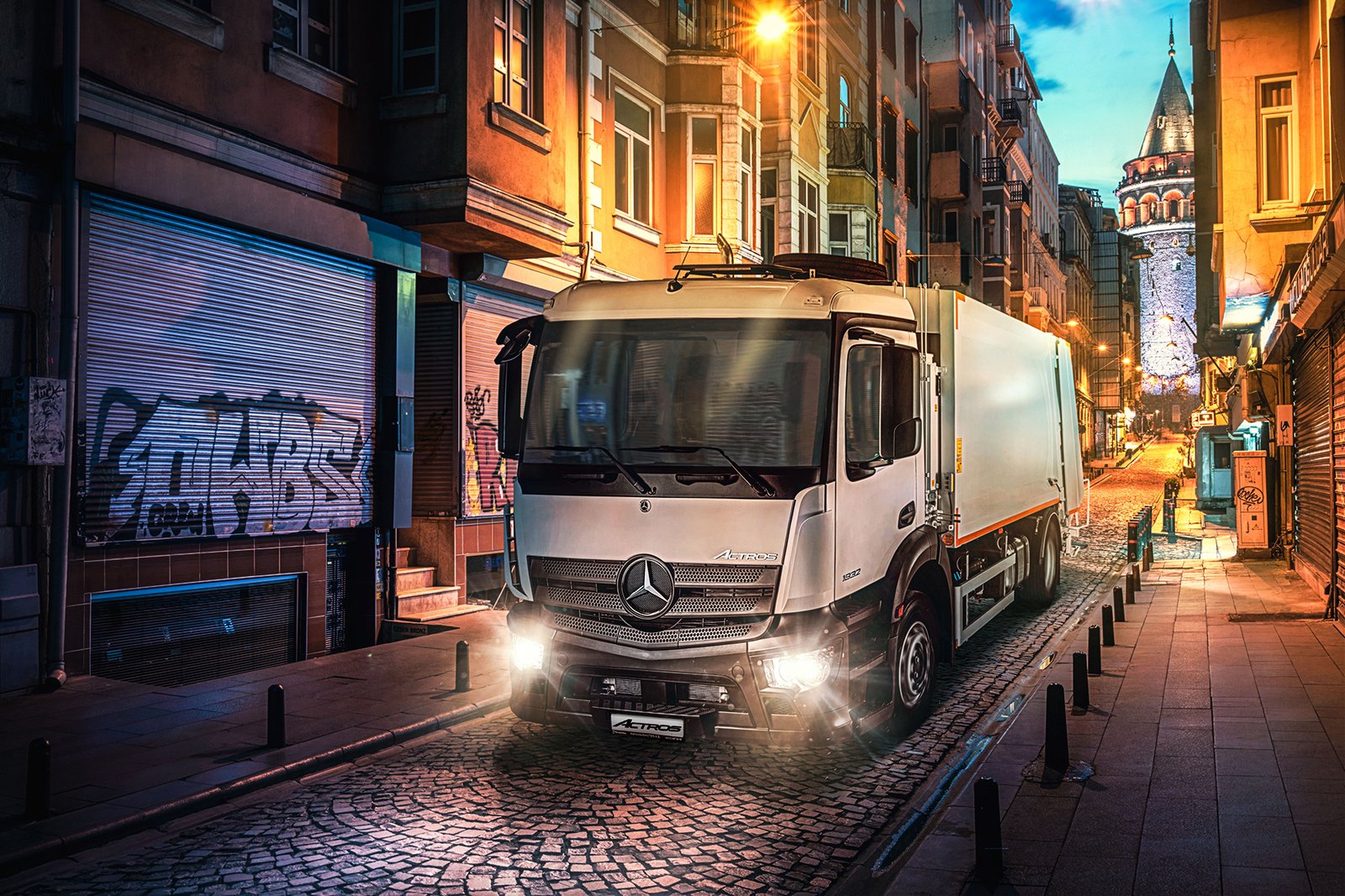 A commercial urban night photograph by Sinan Niyazi Kutsal capturing a white Mercedes-Benz Actros specialty utility truck on an old cobblestone street in Istanbul, with the historic Galata Tower glowing in the background.