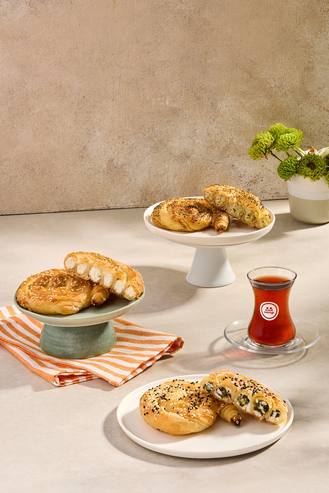 Studio photograph of Simit Sarayı mini gül böreği pastries served with Turkish tea, arranged on ceramic stands under hard daylight-style flash lighting.