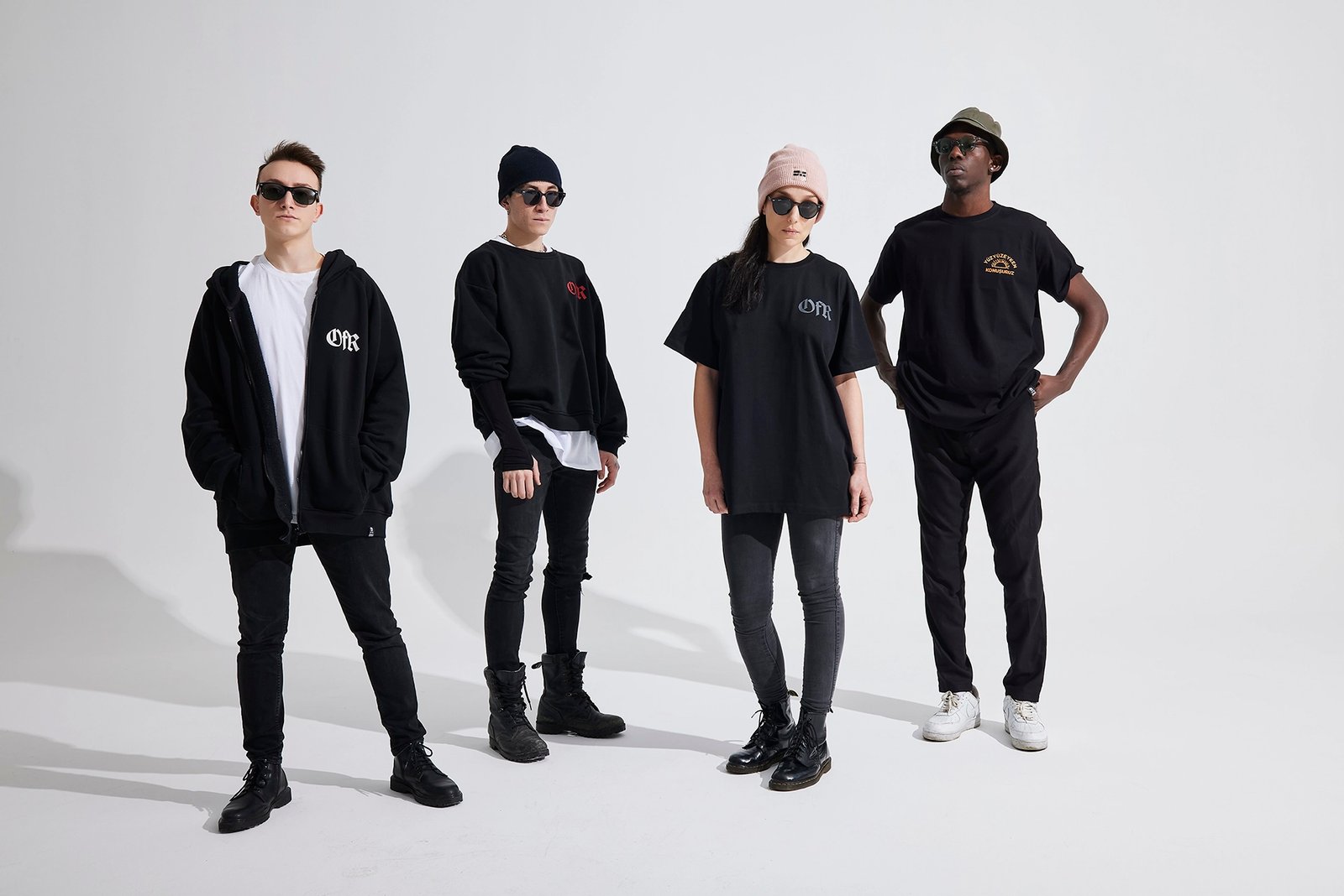 A professional fashion catalog group shot by Sinan Niyazi Kutsal showing four diverse models lined up against a bright white studio backdrop, wearing the latest black and white winter streetwear apparel from Outfit For Rockstars.