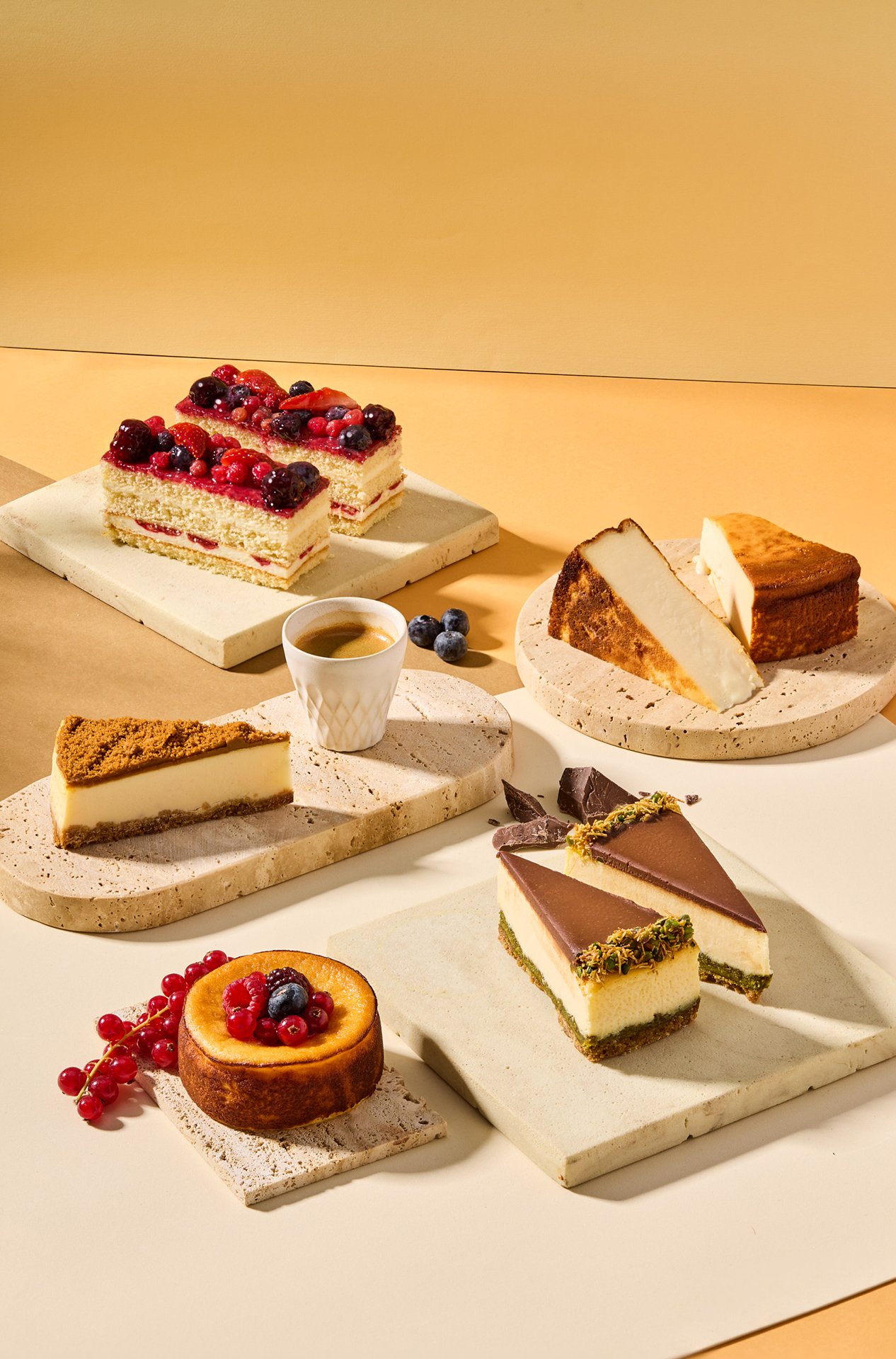 Studio photograph featuring a selection of Simit Sarayı cheesecakes and dessert slices arranged on stone platforms under hard daylight-style flash lighting.