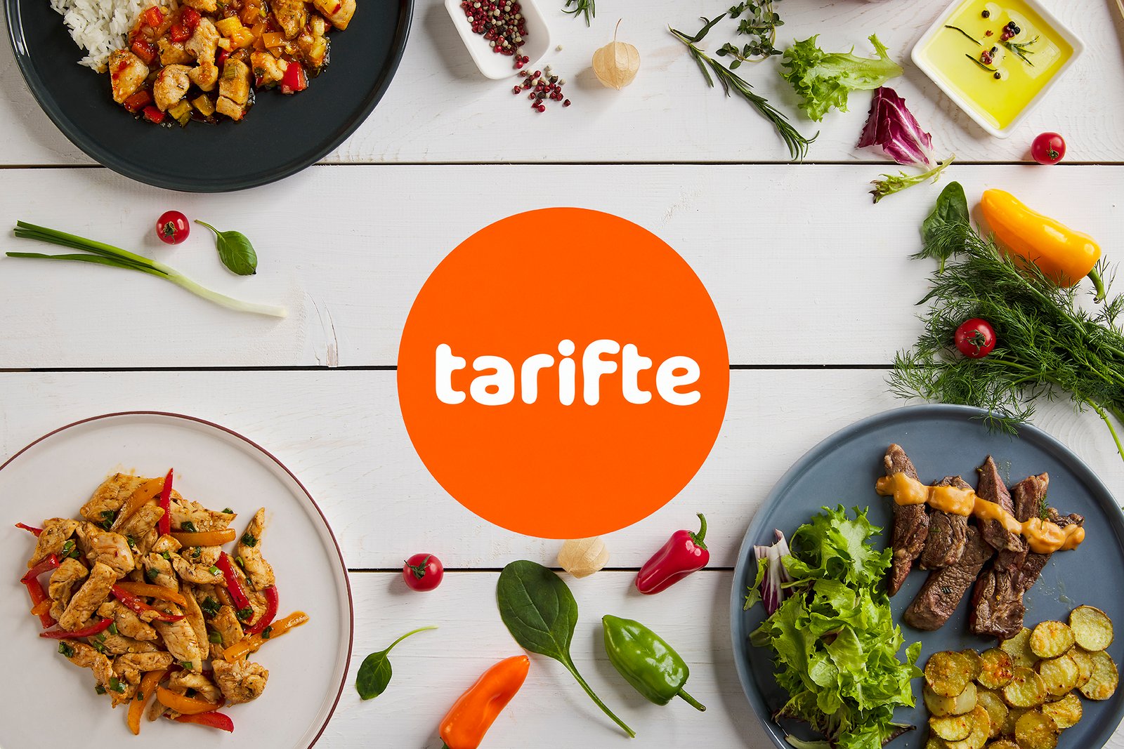 Professional commercial food advertising photograph by Sinan Niyazi Kutsal for Tarifte, featuring a wide top-down view of multiple plates of chicken, steak, and vegetables arranged around a large orange circular brand logo on white wood boards.